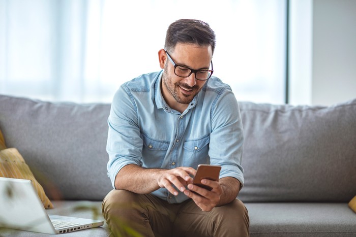 Smiling Man Using Smartphone on Sofa