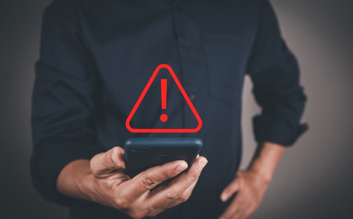 Man in Blue Shirt Holding Phone with Red Warning Triangle