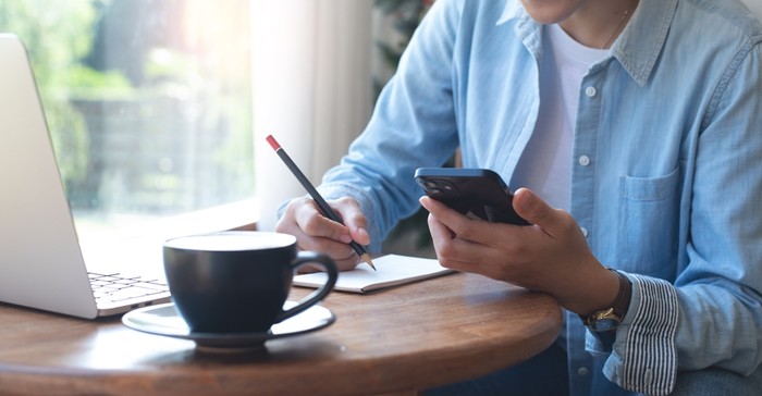 Man with Phone Writing in Notepad