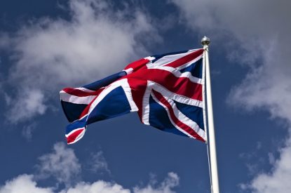 UK Flag on Pole Against Blue Cloudy Sky