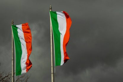 Two Ireland Flags Against Dark Grey Skies