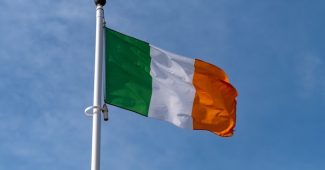 Irish Flag on White Pole Against Blue Cloudy Sky