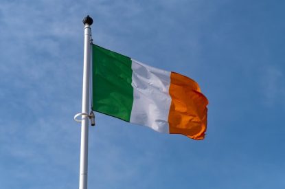 Irish Flag on White Pole Against Blue Cloudy Sky