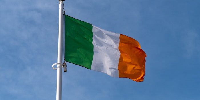 Irish Flag on White Pole Against Blue Cloudy Sky