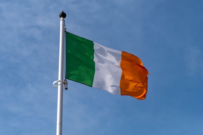 Irish Flag on White Pole Against Blue Cloudy Sky